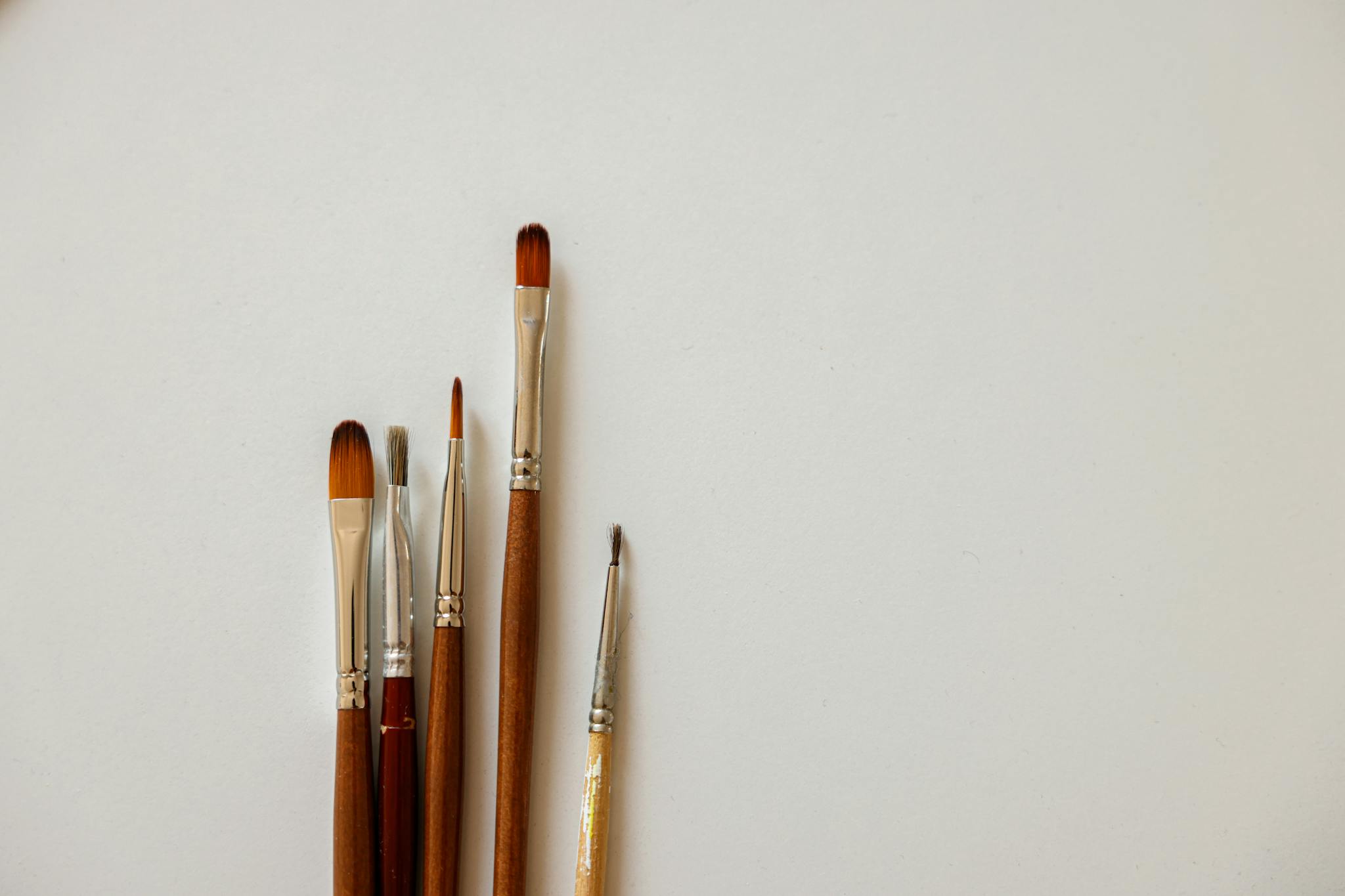 A collection of five paint brushes laid on a clean white surface, ideal for artistic purposes.
